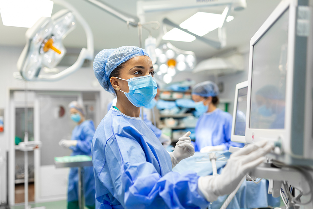 Worker wearing Protective Gear checking monitors while sedating patient before surgical procedure in hospital